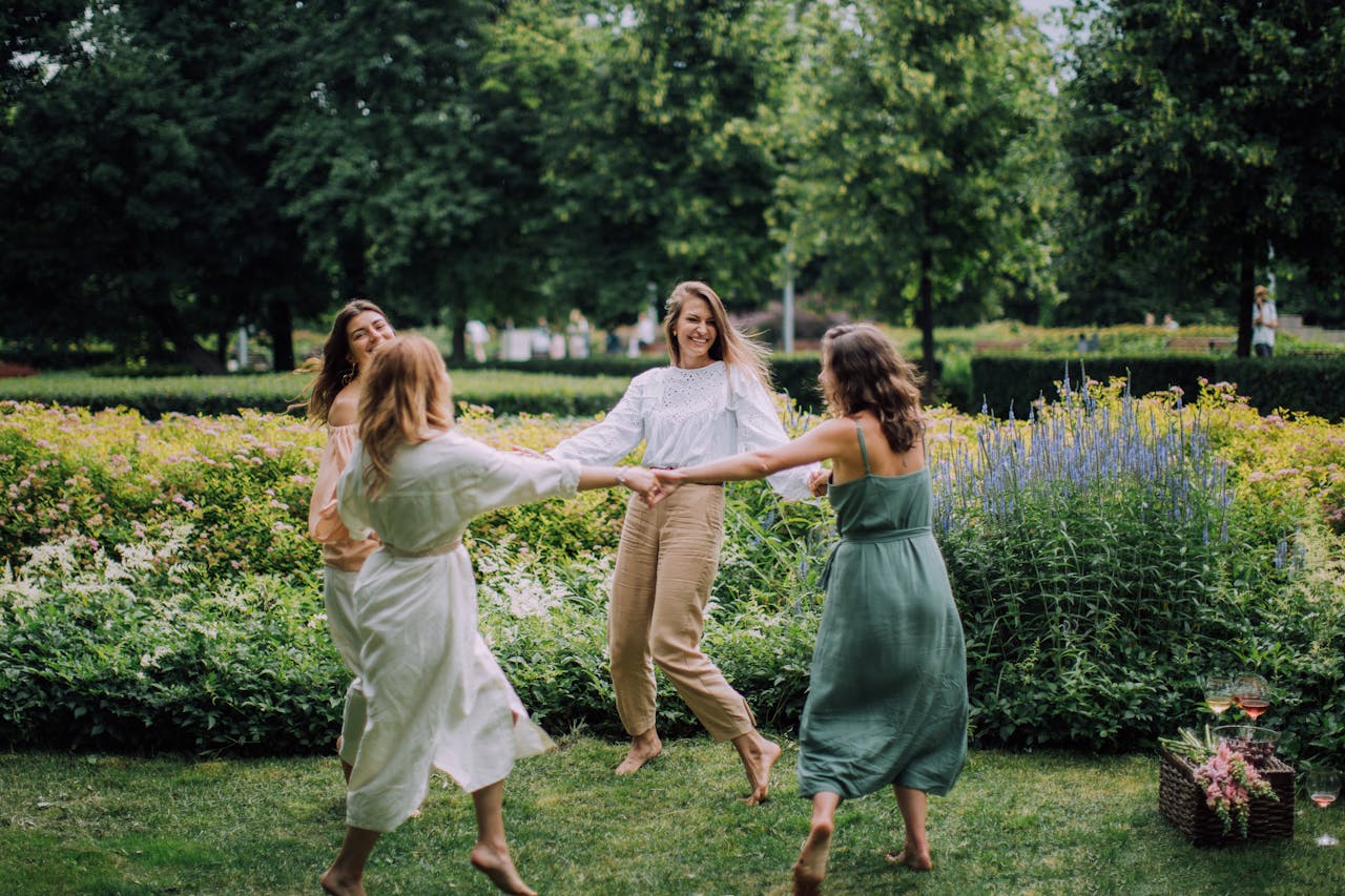 about-us A group of women joyfully dancing in a park on a summer day, exuding happiness.